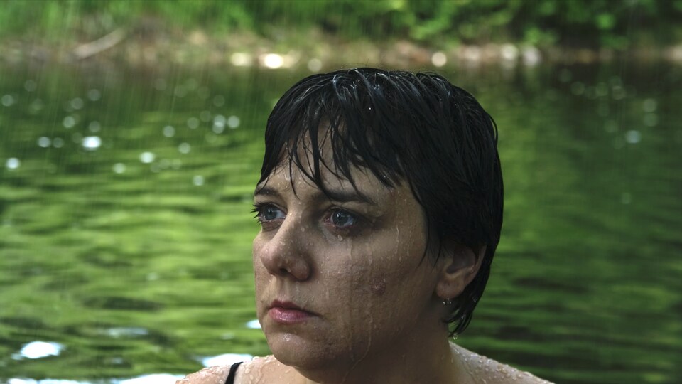 Une femme est debout dans l'eau d'un lac ou d'un étang; il pleut.