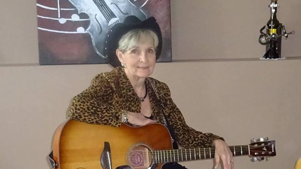 Une femme portant un chapeau de cowboy est assise avec une guitare dans son salon.
