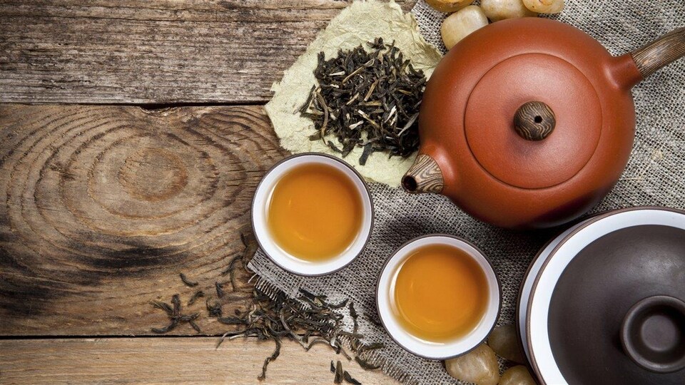 Deux théières, deux tasses de thé et des feuilles de thé sur une surface en bois