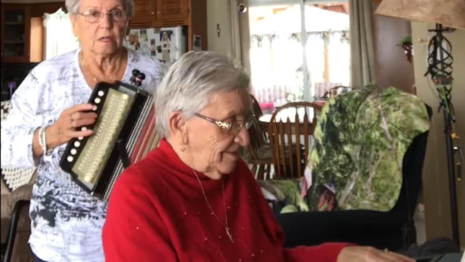 Deux soeurs âgées de 89 et 85 ans regardent la caméra. Jeannette Filion joue de l'accordéon et sa soeur Thérèse l'accompagne au clavier électronique.