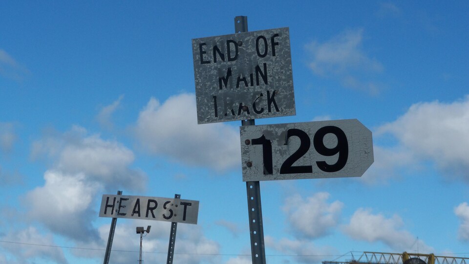 Trois panneaux de signalisations où sont inscrits, respectivement, « Hearst », « End of Main Track » et « 129 »