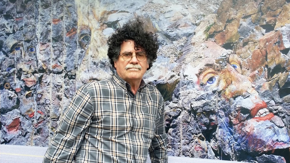 L'artiste Marc Brisson debout devant une de ses œuvres.