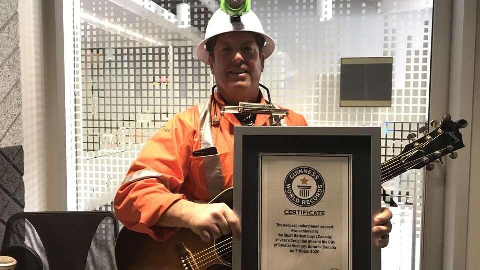 Un homme déguisé en mineur, avec une guitare et un harmonica, tient un certificat encadré des records du livre Guinness.