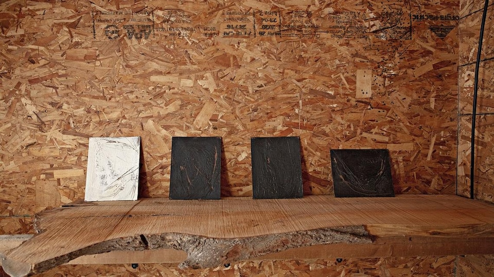 Quatre tableaux à l'encaustique sont installés sur une tablette de bois 