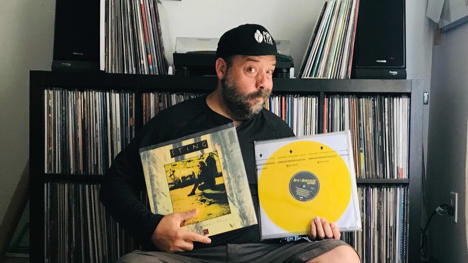 Stef Paquette devant sa collection de vinyles et sa table tournante. Il a un disque de Sting et un disque d'Amy Winehouse entre les mains.