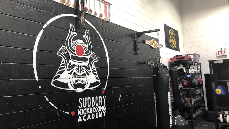 L'un des murs à la Sudbury Kickboxing Academy où l'on voit le logo de l'entreprise, des médailles et de l'équipement sportif.
