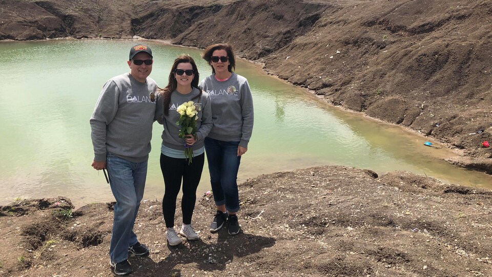 Sylvie Lamarche Lacroix, son conjoint Alain Lacroix et leur fille Dominique sont debout sur les lieux de l'écrasement d'avion du Boeing 737 Max de Ethiopian Airlines. L'eau de couleur turquoise en arrière de la famille de Stéphanie Lacroix. Dominique tient un bouquet de roses blanches.
