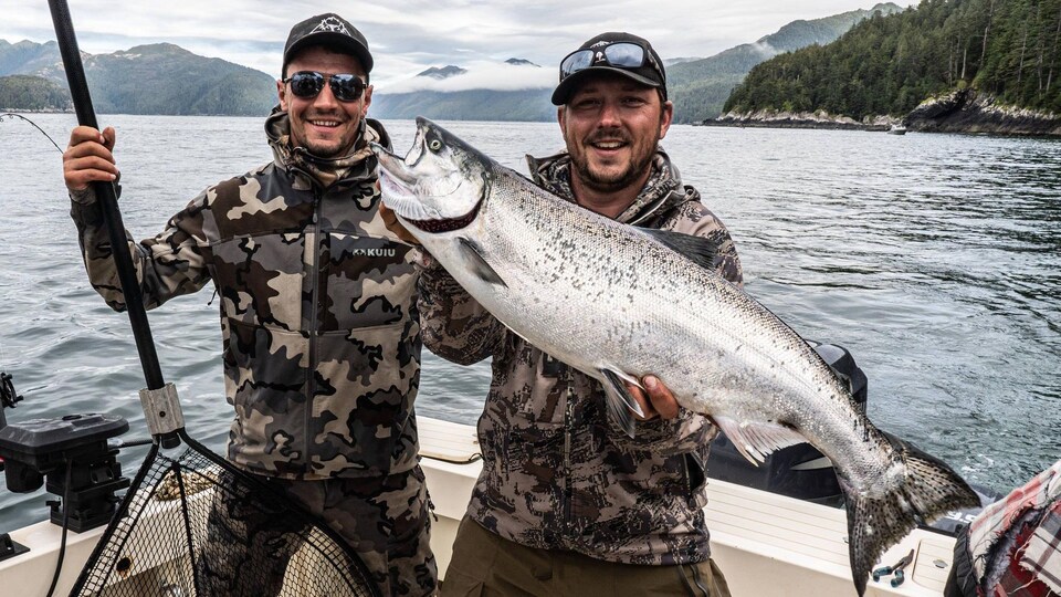 Les deux hommes debout sur un bateau. Travis Vernier tient le saumon dans ses mains.