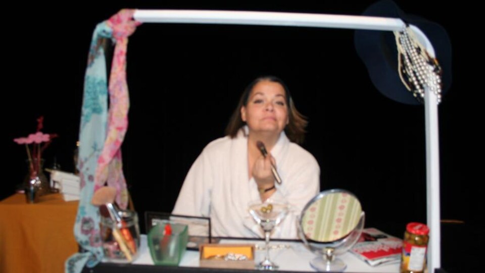 Une comédienne se maquille devant un faux-miroir dans un décor de théâtre.