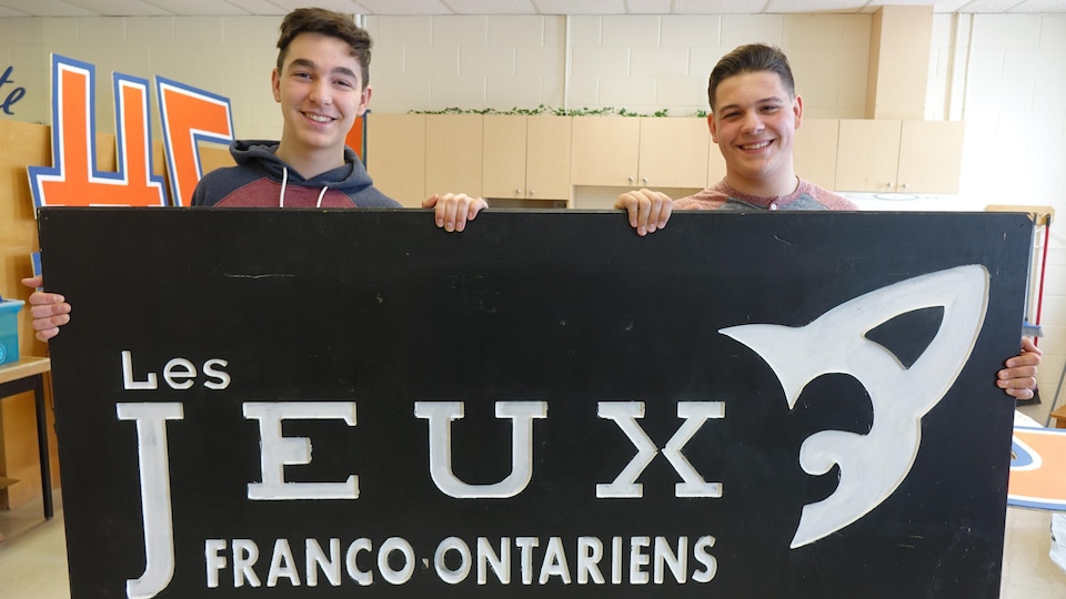 Médéric Bourdon et Cameron Wahl tiennent une grande pancarte des Jeux franco-ontariens