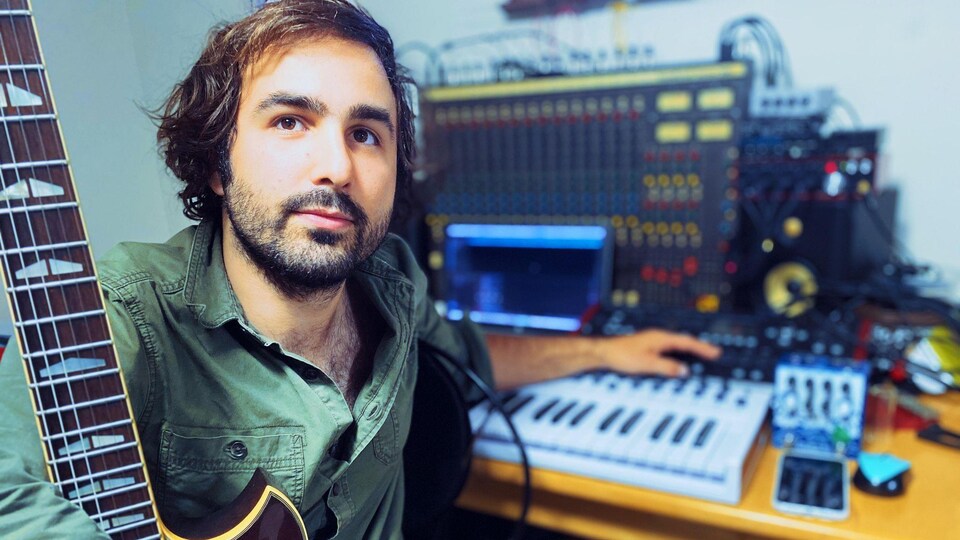 Un homme tient une guitare et manipule une console de son.