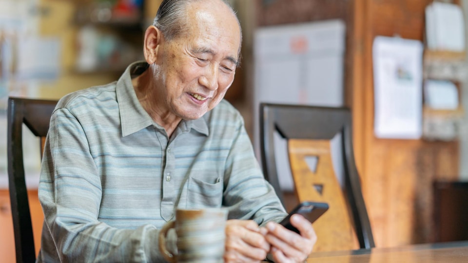Un homme âgé manipule son téléphone cellulaire en souriant.