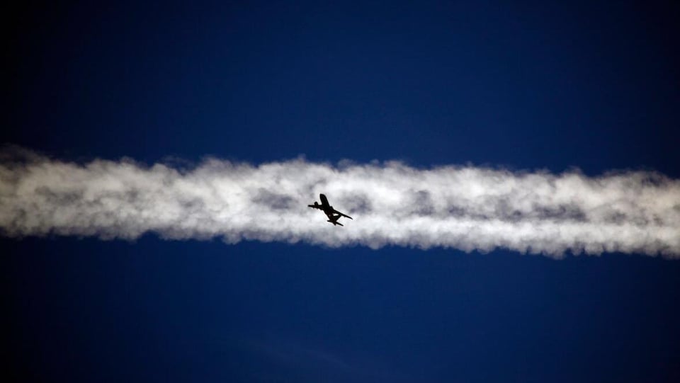 Un avion au centre d'une traînée blanche dans le ciel.