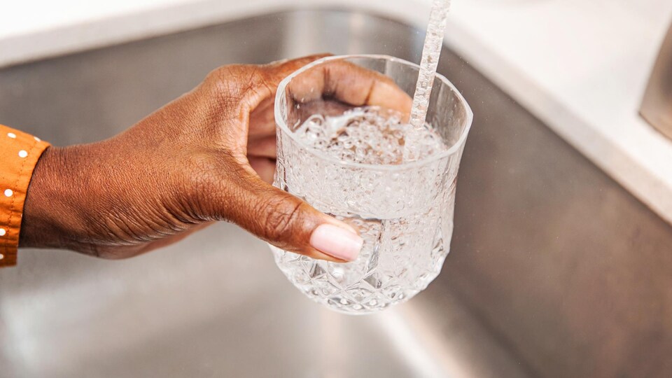 Une personne se sert un verre d'eau directement du robinet.