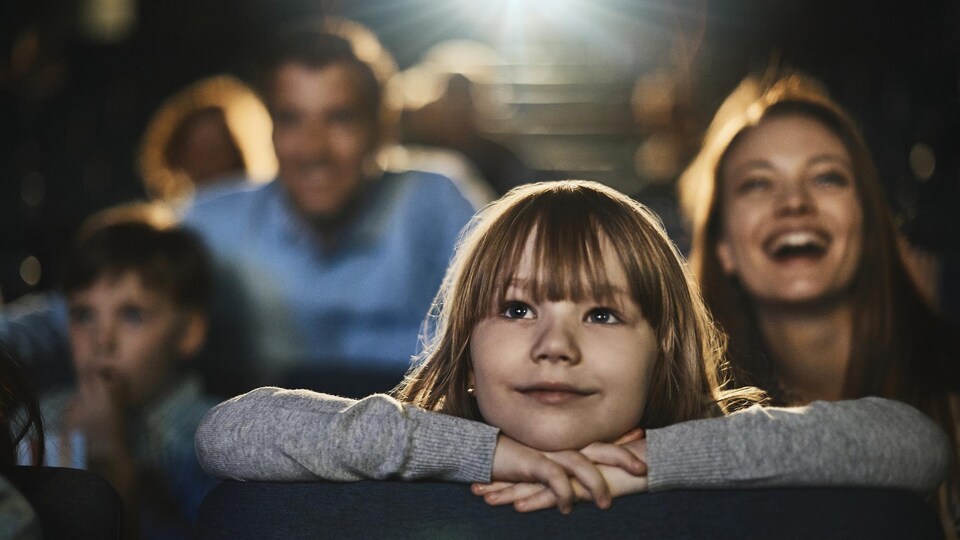Une fillette prend plaisir à regarder un film au cinéma.