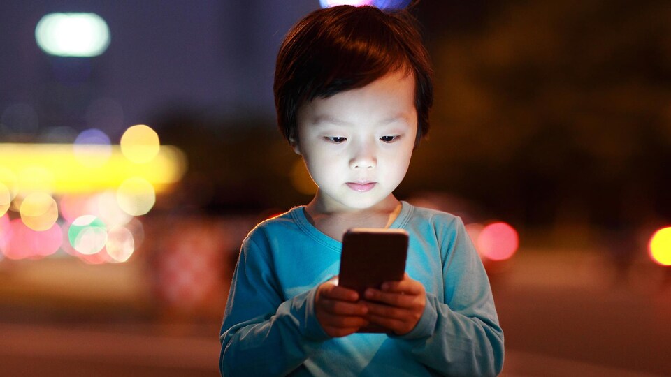 Un bambin est captivé par l'écran d'un téléphone portable.