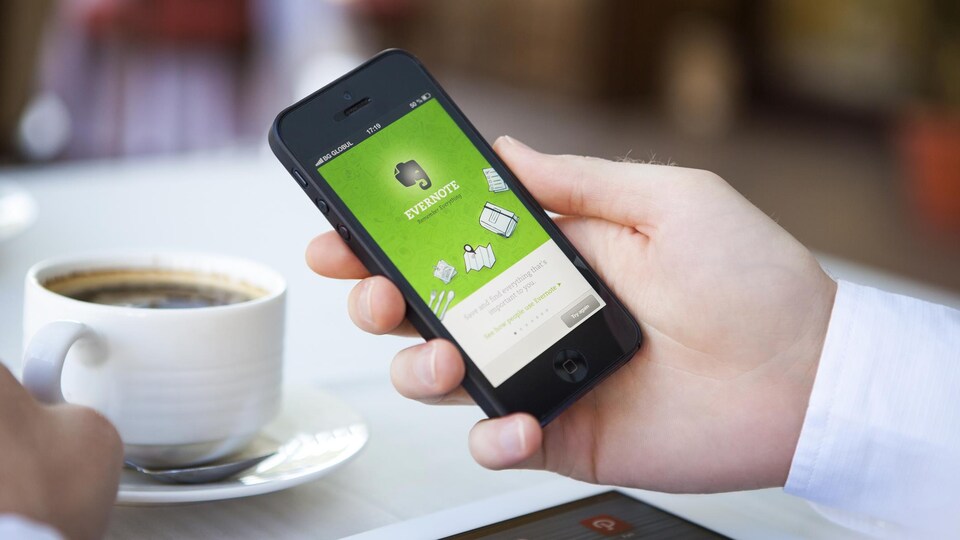 Une personne consulte l'application Evernote avec son téléphone intelligent en buvant un café.