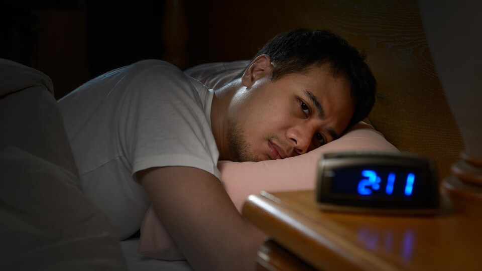 Un homme souffrant d'insomnie regarde mélancoliquement son réveil depuis son lit.