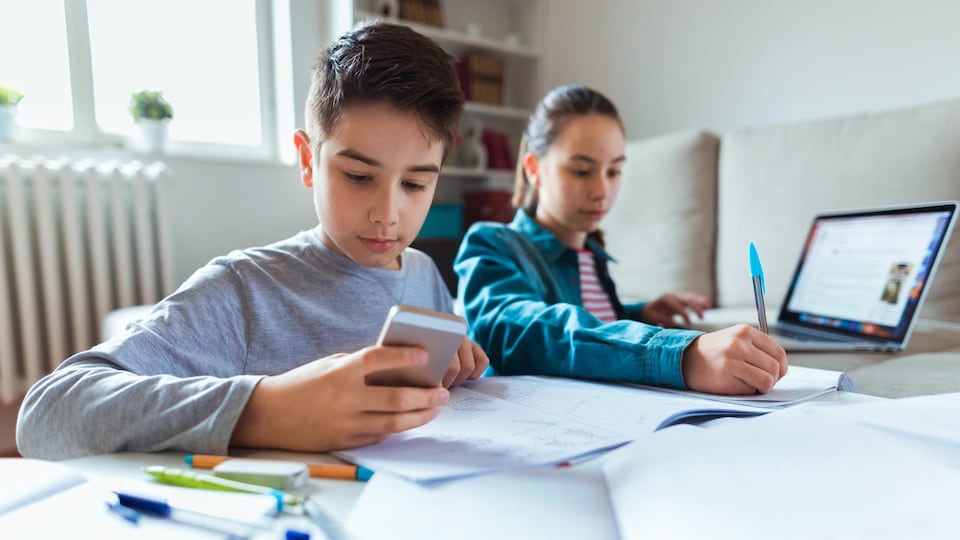 Deux adolescents font leurs devoirs à l'aide d'un ordinateur et d'un téléphone cellulaire.