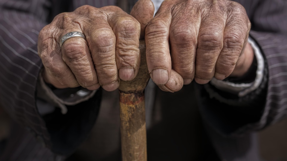 Les mains d'un homme âgé appuyées sur une canne.