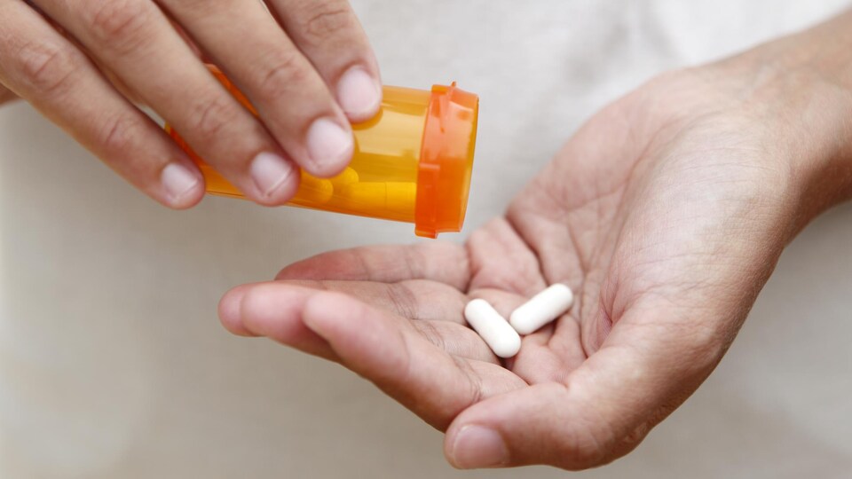 Une personne verse quelques médicaments dans sa main gauche.