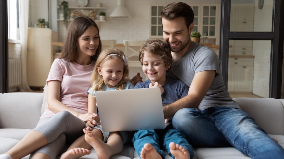 Une jeune famille heureuse avec des enfants regarde une vidéo sur un ordinateur portable.