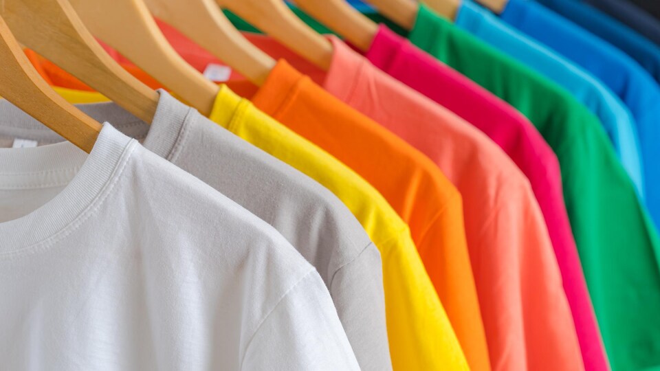 Des t-shirts de couleurs différentes sont accrochés à un support à l'aide de cintres en bois.