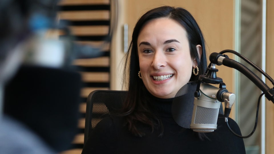 Une femme sourit derrière un micro dans un studio de radio lors d'une entrevue. 