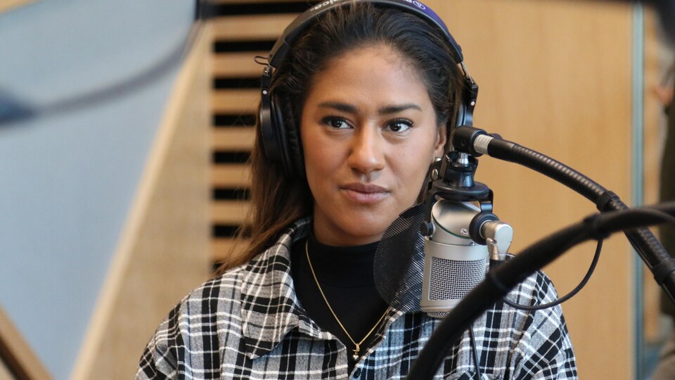 Une femme, casque d'écoute sur la tête, regarde dans la direction de l'animateur dans un studio de radio.  