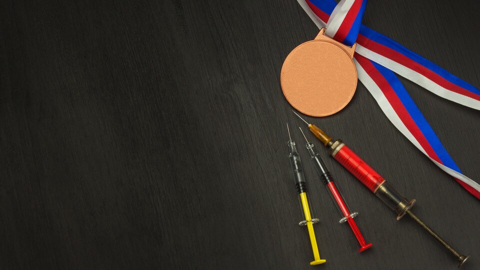 Trois seringues disposées sur une surface noire à côté d'une médaille et son ruban.