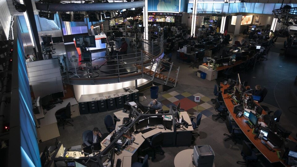 Une salle de rédaction avec des journalistes à leurs bureaux et un plateau de télévision.