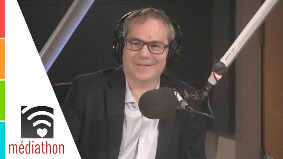 Homme dans la mi-quarantaine avec lunettes devant un micro.