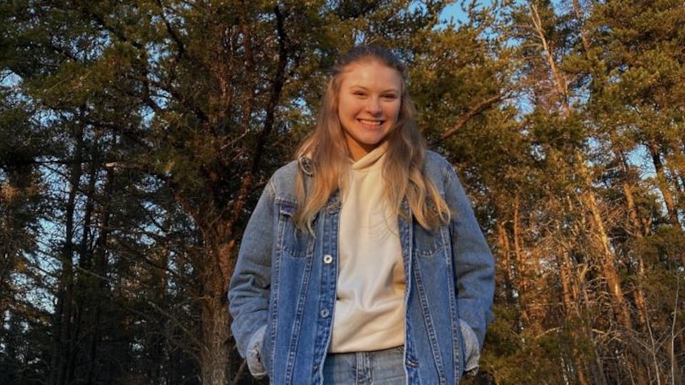 Une adolescente souriante debout devant des arbres.
