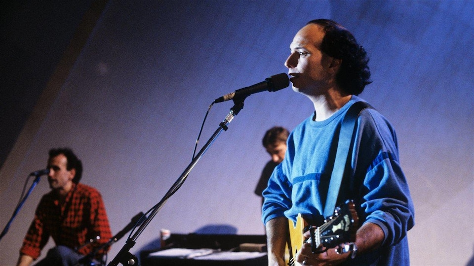 Michel Rivard chante avec deux musiciens.