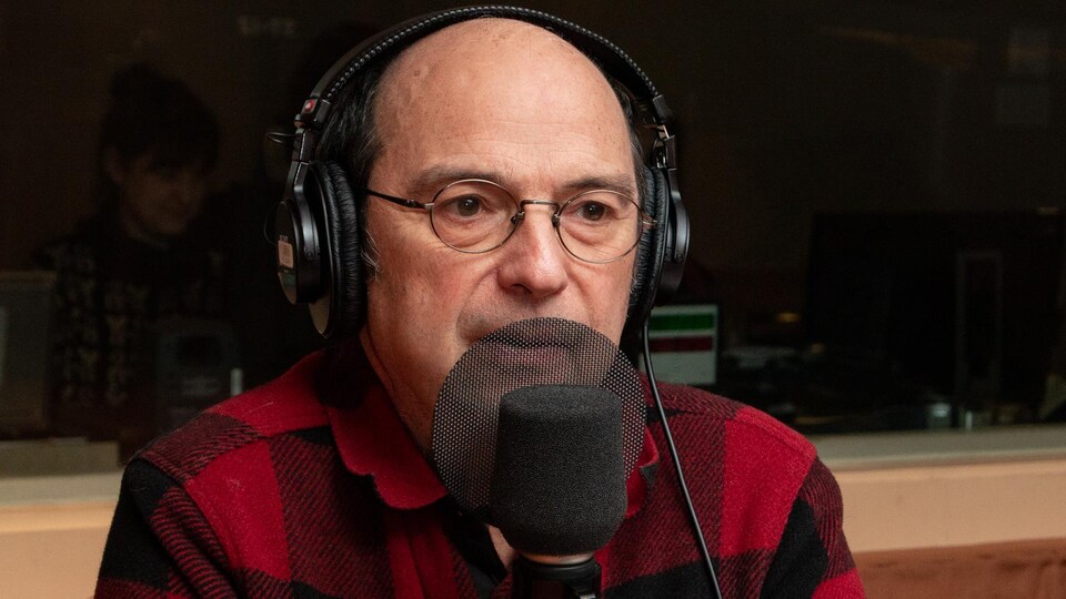 Devant le micro, le musicien est affublé d'une veste à carreaux rouges et noirs.