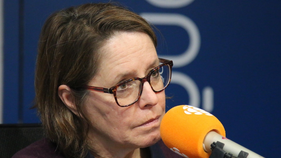 Une femme aux cheveux courts et portant des lunettes de vues parle au micro.