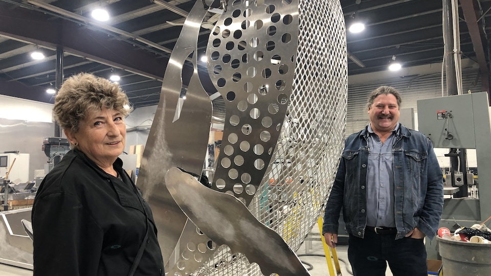 Michelle Lefort et Stéphane Bergeron devant la sculpture métallique en forme de baleine, dans un atelier de soudure.