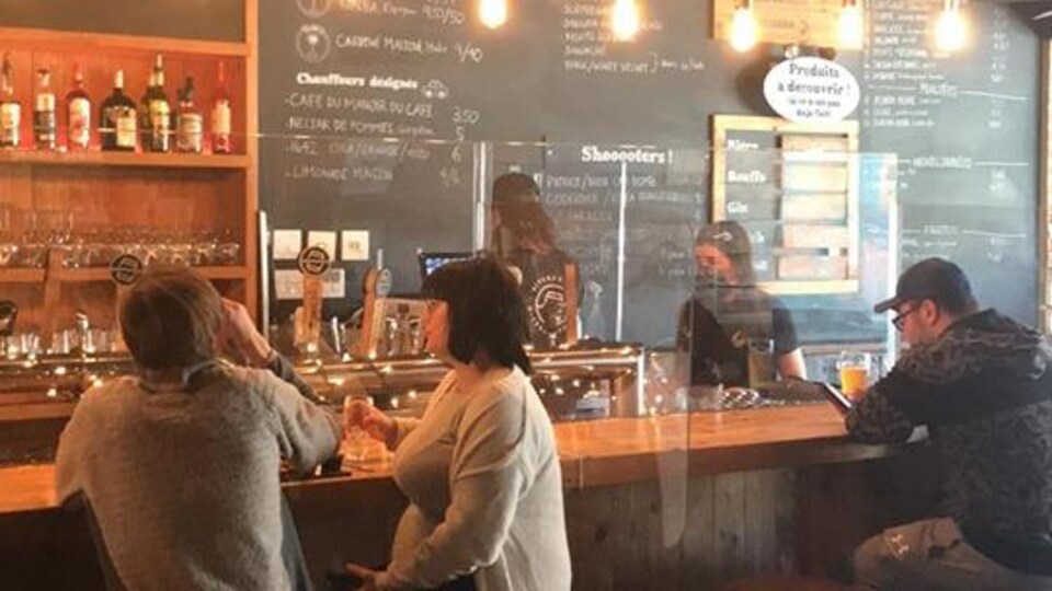 Un bar avec des gens assis au comptoir devant des panneaux de plexiglass