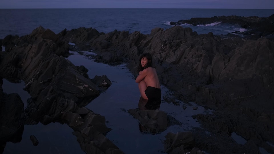 Une femme sur les rochers en bord de mer à moitié nue cache son corps
