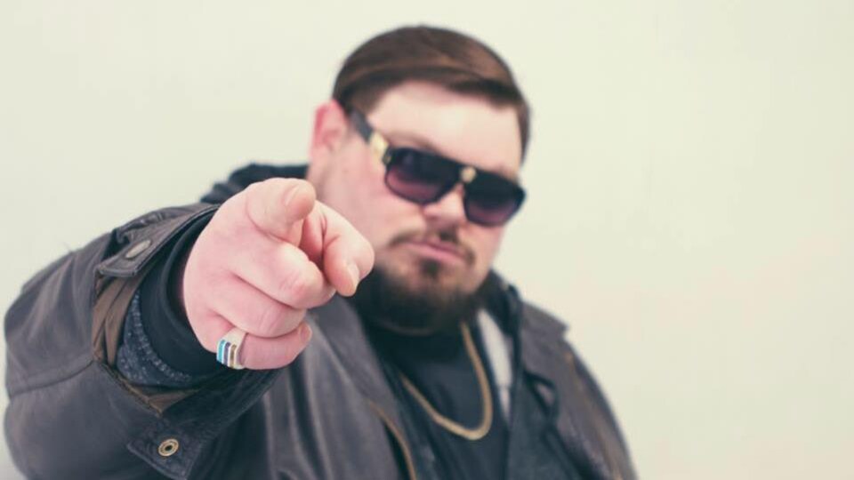 Mike à Vik est sérieux et porte un manteau de cuir avec des lunettes fumées. Il pointe l'objectif de la caméra avec attitude et détermination.