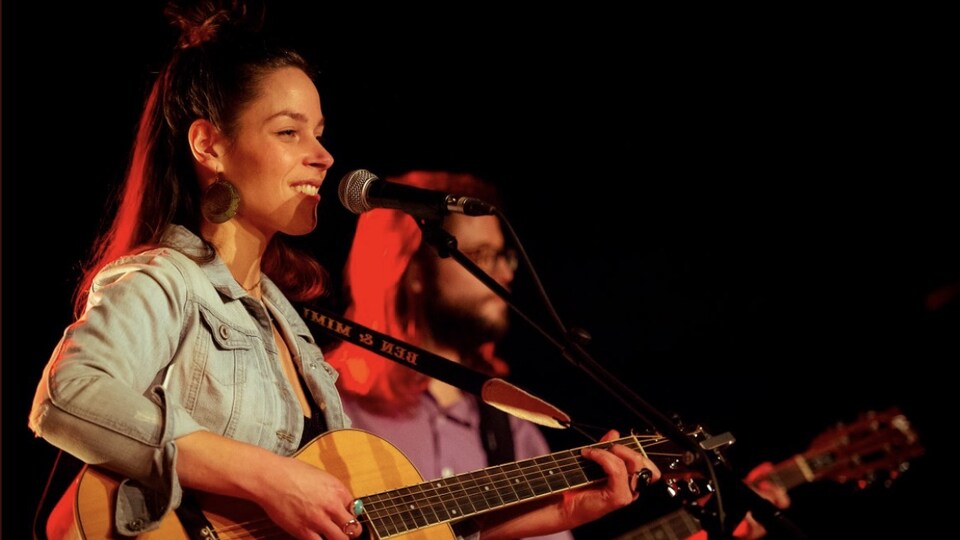 Mireille chante sur scène avec sa guitare. Elle est accompagnée d'un autre guitariste.