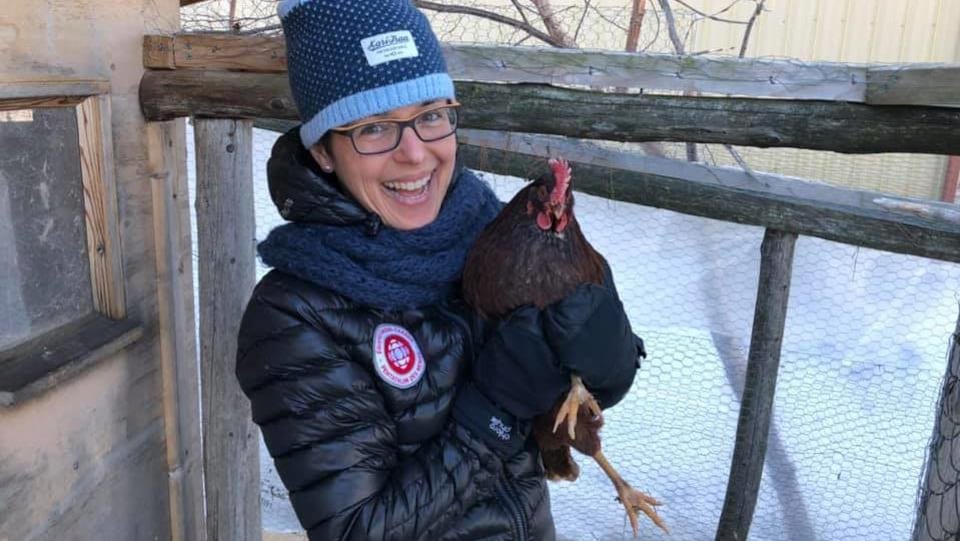 Dans un modeste poulailler, Mireille tient une poule dans ses bras