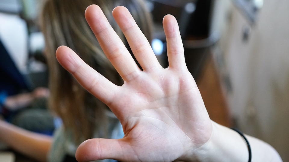 Une femme met sa main entre elle et l'objectif de la caméra.