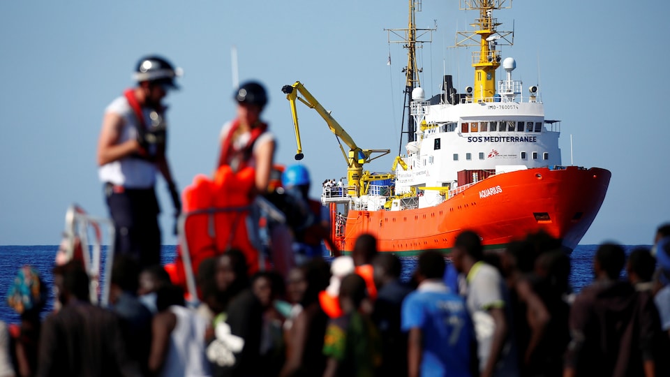 Des migrants attendent sur une embarcation en pleine mer Méditerranée.