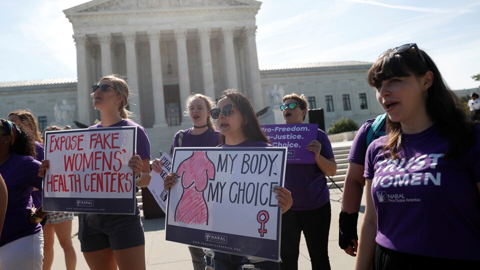 Quelques femmes vêtues de violet manifestent leur position en faveur de l'avortement en brandissant des pancartes sur lesquelles on peut lire « Démasquez les faux centres de santé des femmes » ou « Mon corps mon choix ».