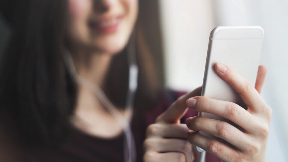 Une jeune femme sourit en tenant un téléphone intelligent et en portant des écouteurs