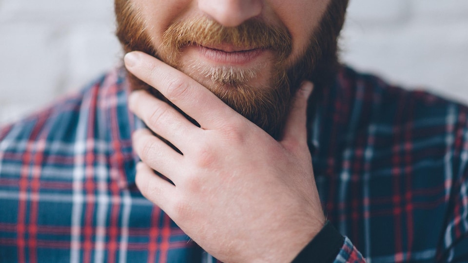 Bas du visage d'un jeune homme se frottant la barbe.