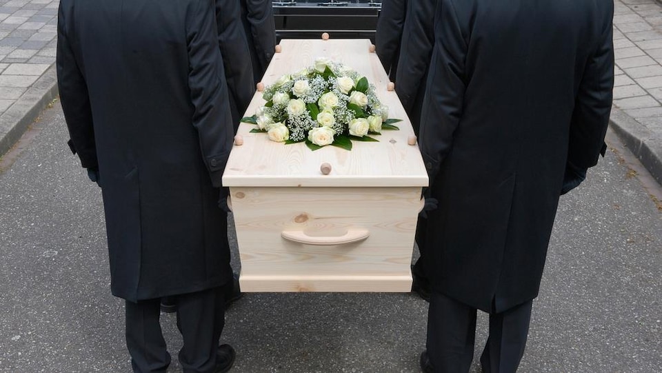 Des porteurs déposent un cercueil dans un corbillard.