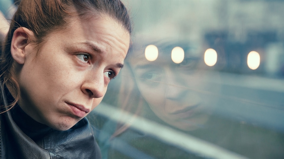 Une femme assise dans un transport en commun regarde par la fenêtre.