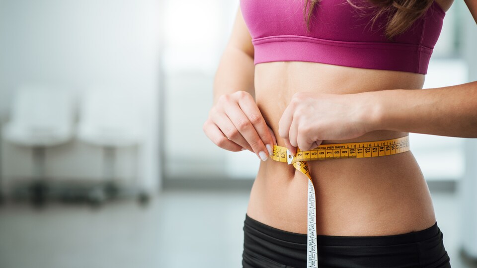 Une femme mesure son tour de taille au moyen d'un ruban à mesurer.